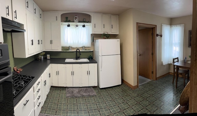 kitchen featuring under cabinet range hood, a sink, white cabinetry, freestanding refrigerator, and dark countertops