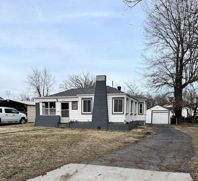 view of front of home with entry steps, a detached garage, aphalt driveway, roof with shingles, and an outdoor structure