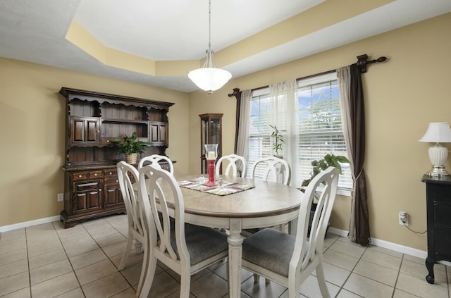 dining area featuring a raised ceiling, baseboards, and light tile patterned floors