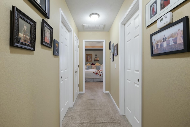 corridor with baseboards, visible vents, and carpet flooring