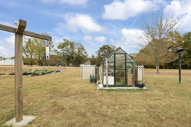 view of yard featuring fence, a greenhouse, and an outbuilding