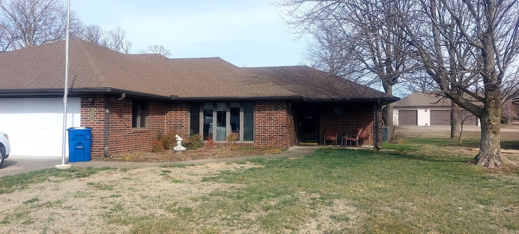 ranch-style house featuring a garage, a front yard, brick siding, and roof with shingles