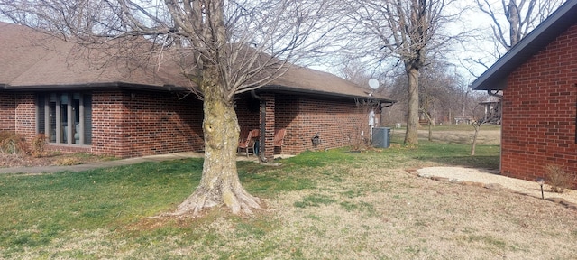 view of side of property featuring roof with shingles, cooling unit, a lawn, and brick siding