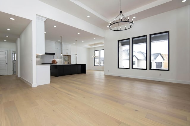 unfurnished living room with an inviting chandelier, baseboards, light wood-style floors, and recessed lighting