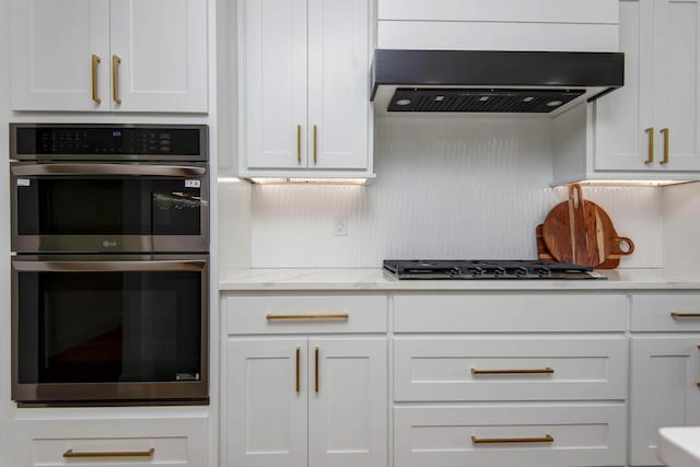 kitchen with black gas cooktop, light stone counters, stainless steel double oven, white cabinetry, and ventilation hood