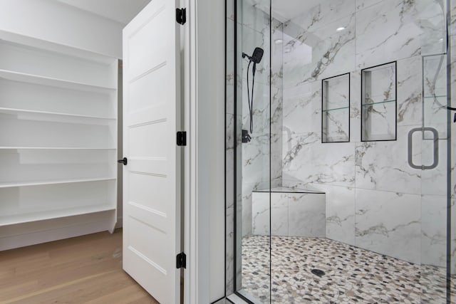 full bathroom with a marble finish shower and wood finished floors