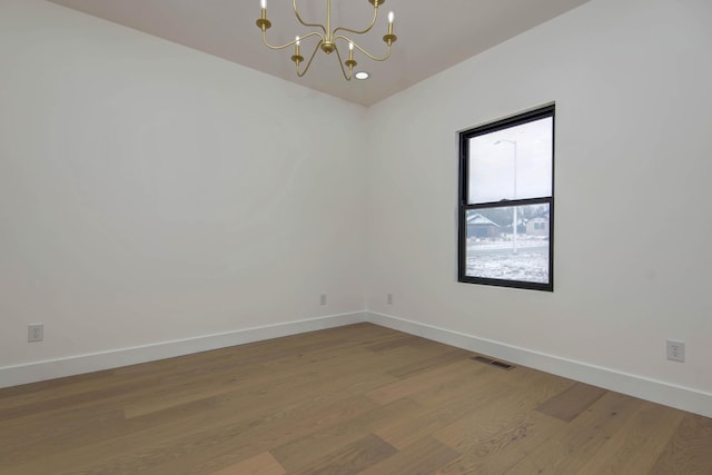 empty room with baseboards, light wood finished floors, visible vents, and an inviting chandelier