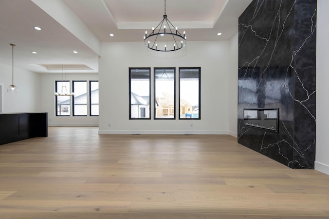 unfurnished living room with baseboards, a raised ceiling, an inviting chandelier, and wood finished floors