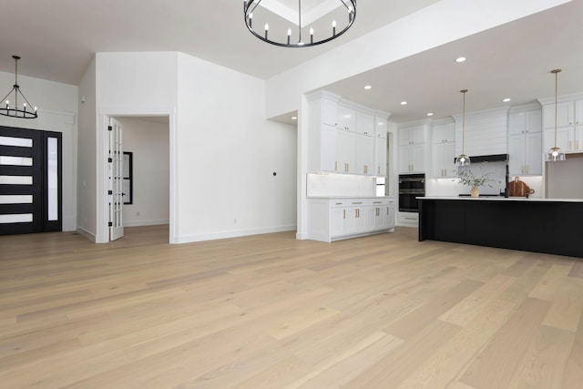 interior space with a notable chandelier, light countertops, hanging light fixtures, stainless steel double oven, and light wood-type flooring