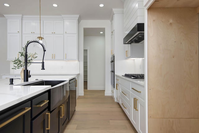 kitchen featuring appliances with stainless steel finishes, white cabinets, a sink, and wall chimney exhaust hood