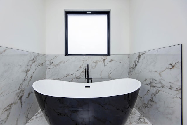 bathroom with marble finish floor, a wainscoted wall, and a soaking tub