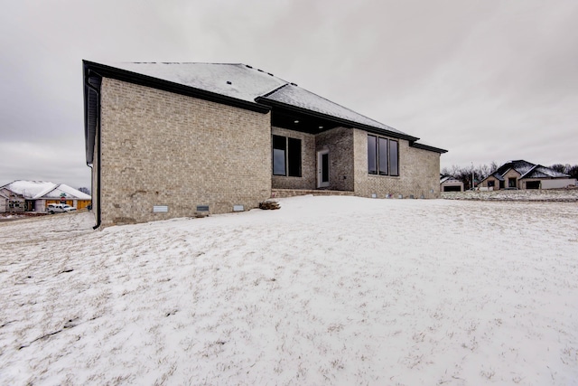 snow covered back of property with crawl space and brick siding