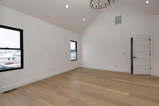 empty room featuring light wood-type flooring, high vaulted ceiling, and visible vents