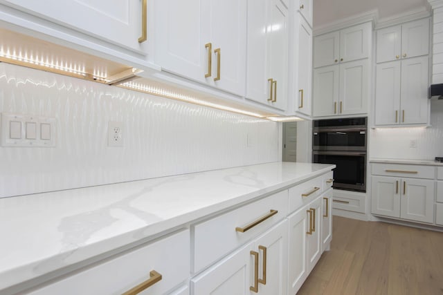 kitchen with double oven, light stone counters, white cabinets, and light wood-style floors