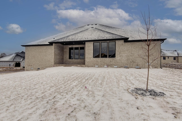 snow covered back of property with crawl space, brick siding, and roof with shingles