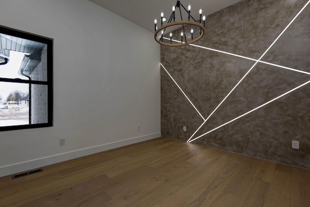 unfurnished dining area featuring baseboards, a notable chandelier, visible vents, and wood finished floors