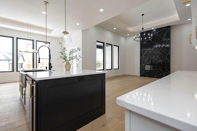 kitchen featuring recessed lighting, dark cabinets, hanging light fixtures, light wood finished floors, and a raised ceiling