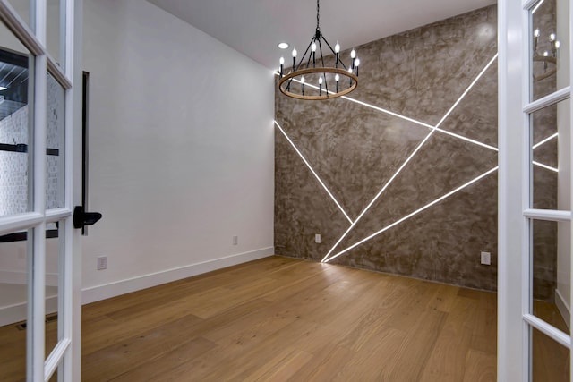 unfurnished dining area with baseboards, an inviting chandelier, and wood finished floors