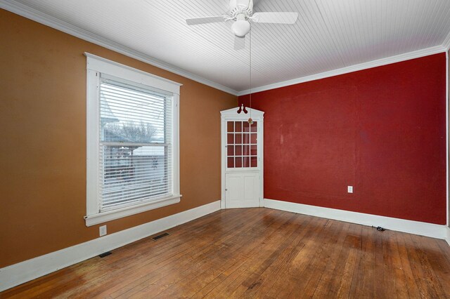 spare room featuring crown molding, wood-type flooring, visible vents, a ceiling fan, and baseboards