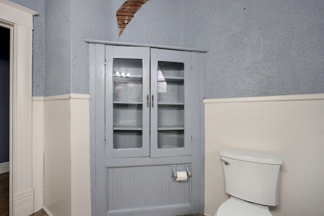 bathroom featuring a textured wall, wainscoting, and toilet