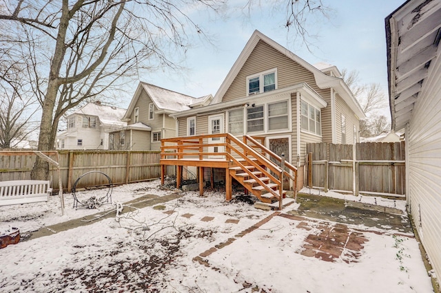 snow covered rear of property with fence and a wooden deck