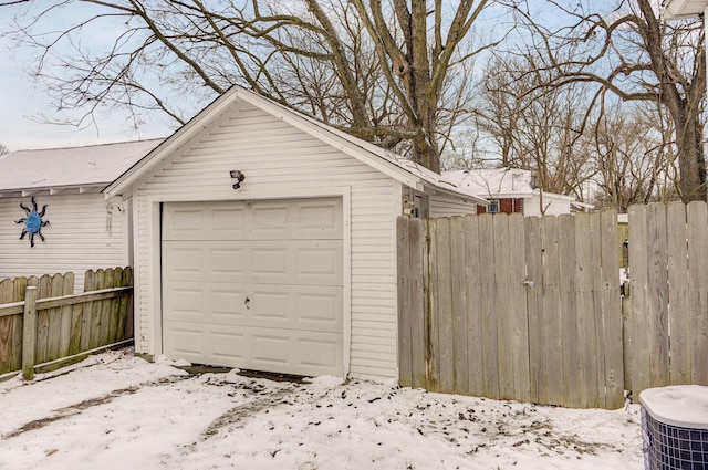 snow covered garage featuring a garage, central air condition unit, and fence