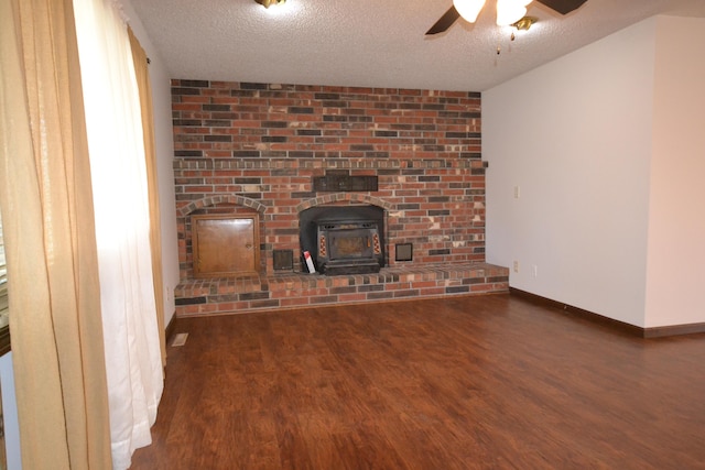 unfurnished living room with baseboards, a wood stove, wood finished floors, a textured ceiling, and a ceiling fan