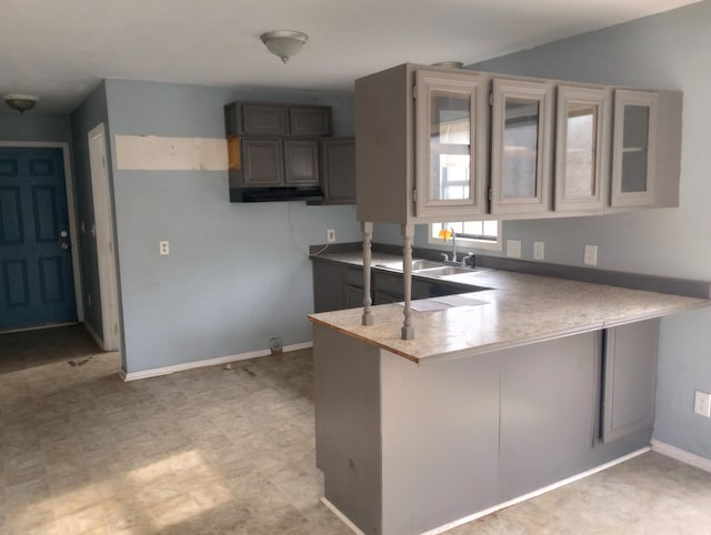 kitchen with baseboards, a peninsula, light countertops, a kitchen bar, and a sink