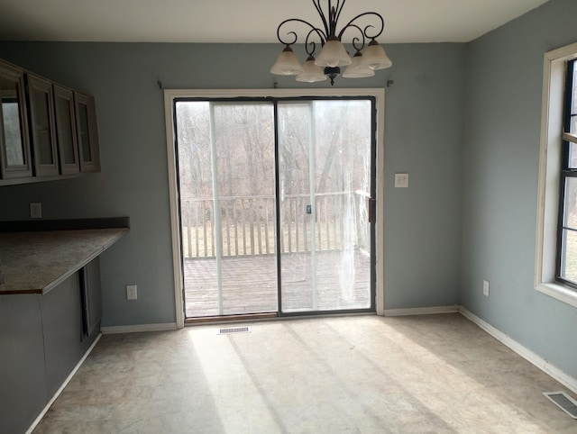 unfurnished dining area featuring baseboards, visible vents, and a notable chandelier