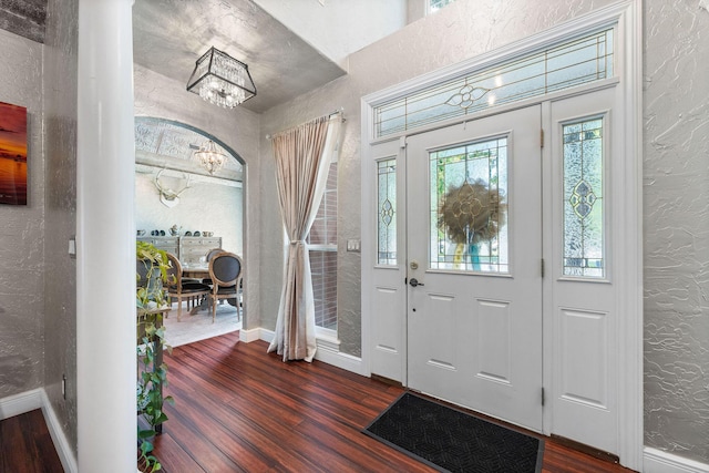 entrance foyer featuring dark wood finished floors, a notable chandelier, a textured wall, and baseboards