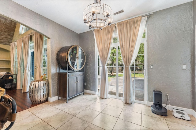 foyer featuring tile patterned floors, a textured wall, baseboards, and an inviting chandelier