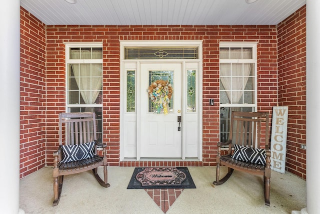 doorway to property with covered porch and brick siding