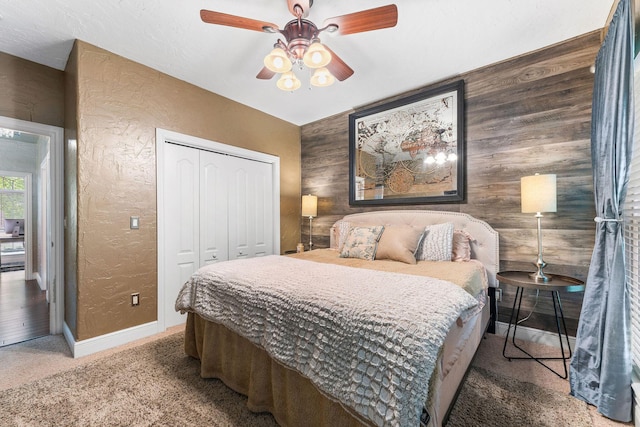 carpeted bedroom with baseboards, a textured wall, ceiling fan, wood walls, and a closet