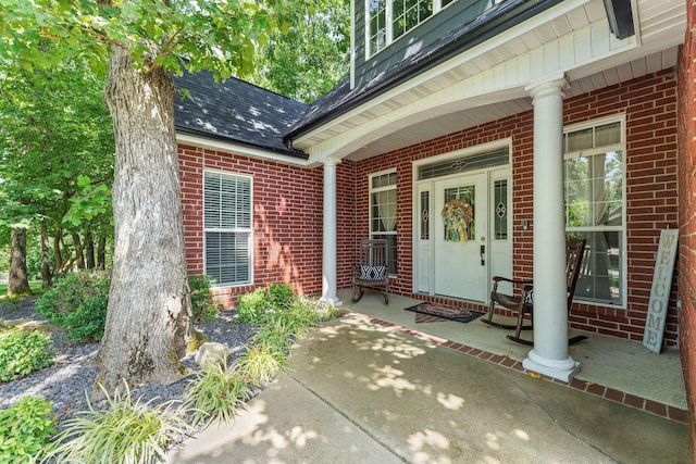 view of exterior entry with a porch, brick siding, and roof with shingles