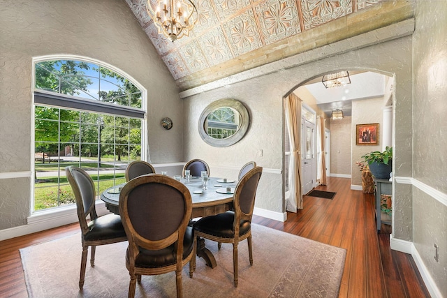 dining room featuring high vaulted ceiling, arched walkways, hardwood / wood-style flooring, and a textured wall