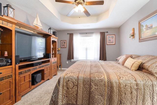 bedroom featuring a raised ceiling, a ceiling fan, and light colored carpet