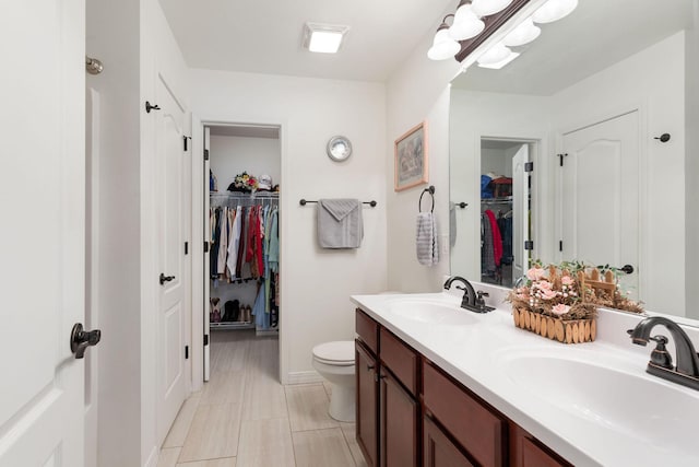 full bath with toilet, a spacious closet, double vanity, and a sink