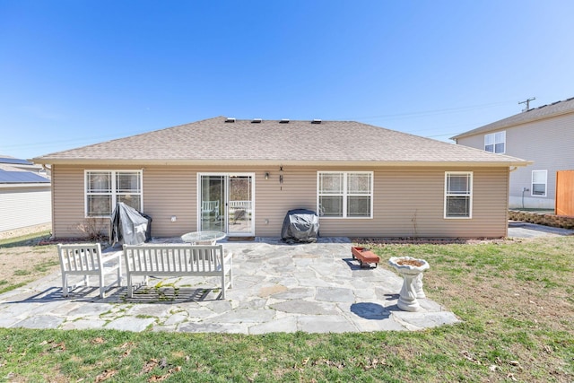 back of property with a shingled roof, a lawn, and a patio area