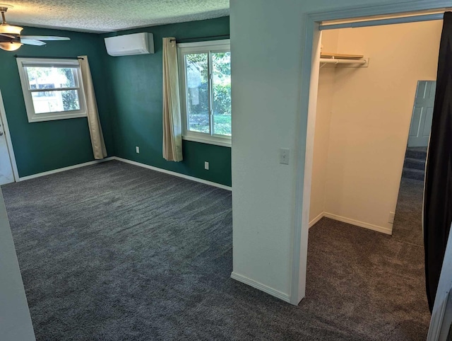 unfurnished bedroom with a textured ceiling, multiple windows, dark carpet, and a wall unit AC