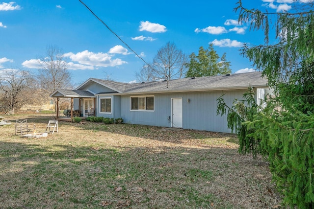 rear view of property featuring a fire pit and a lawn