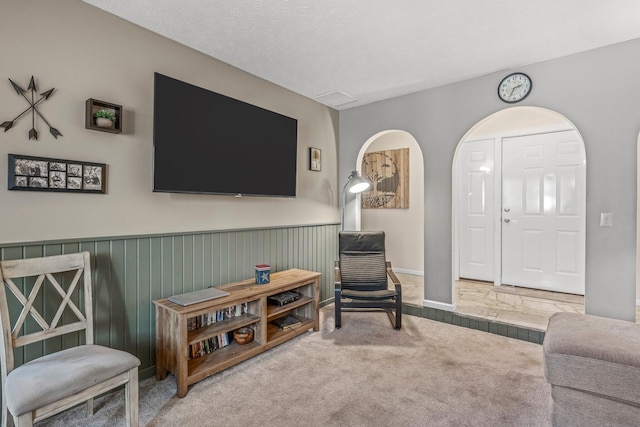 carpeted living area with a textured ceiling and a wainscoted wall