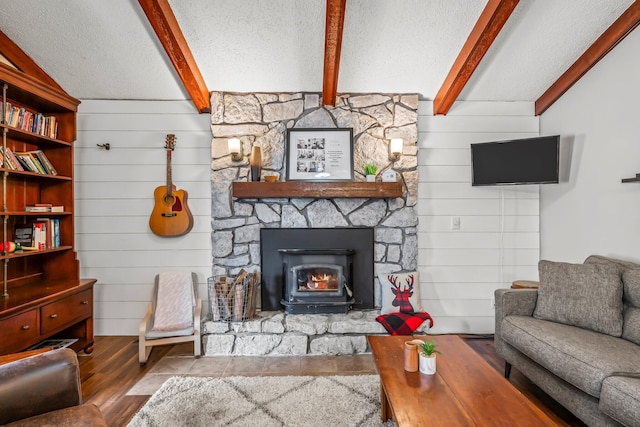 living area featuring a stone fireplace, a textured ceiling, beam ceiling, and wood finished floors