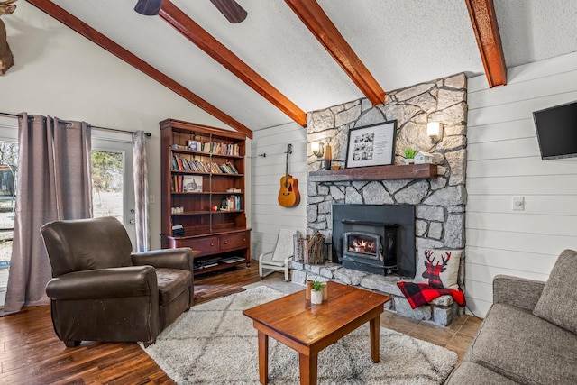 living area with a textured ceiling, lofted ceiling with beams, a stone fireplace, wood walls, and wood finished floors