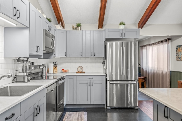 kitchen with dark wood finished floors, appliances with stainless steel finishes, beamed ceiling, gray cabinets, and a sink