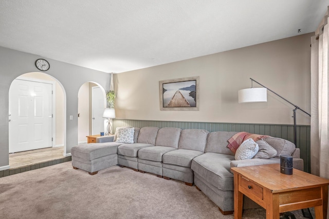 living area featuring arched walkways, a wainscoted wall, and carpet