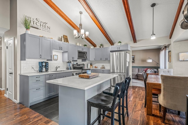 kitchen featuring appliances with stainless steel finishes, gray cabinets, light countertops, and vaulted ceiling with beams