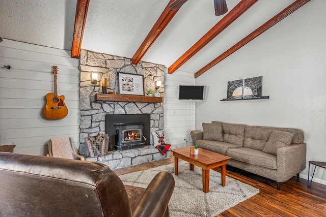 living room featuring lofted ceiling with beams, a stone fireplace, a textured ceiling, wood finished floors, and baseboards