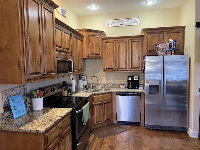 kitchen featuring appliances with stainless steel finishes, dark wood-type flooring, a sink, and light stone counters