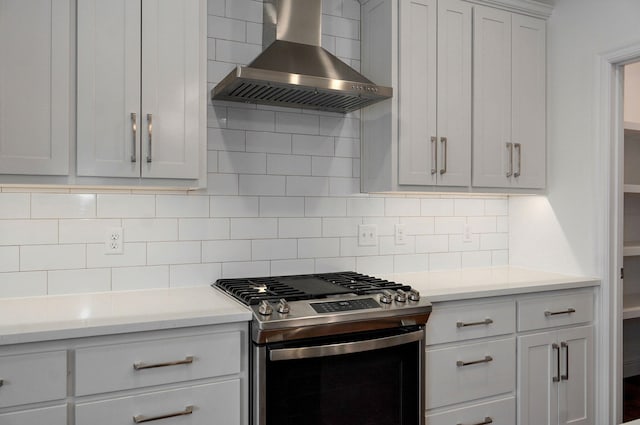 kitchen featuring stainless steel gas range oven, tasteful backsplash, light countertops, wall chimney range hood, and white cabinetry