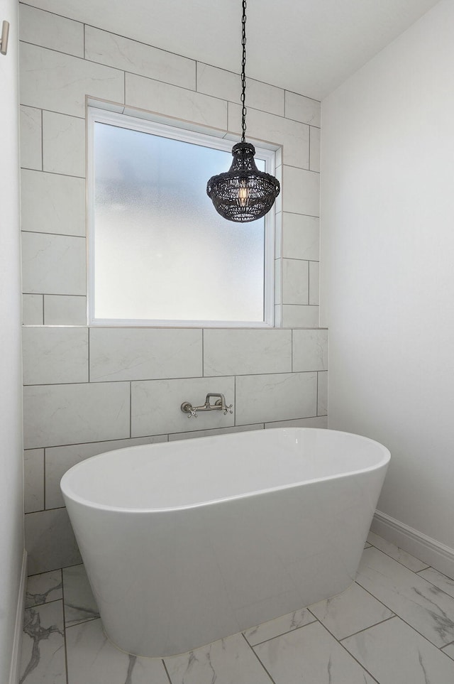 bathroom with marble finish floor, a freestanding tub, and baseboards